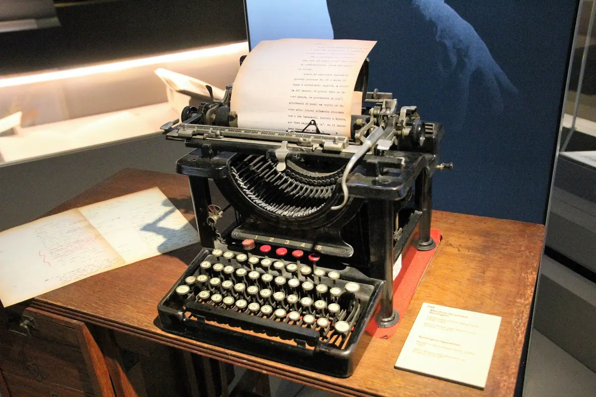 A black Remington typewriter from 1907 on a wooden desk, a sheet of typed paper in it.